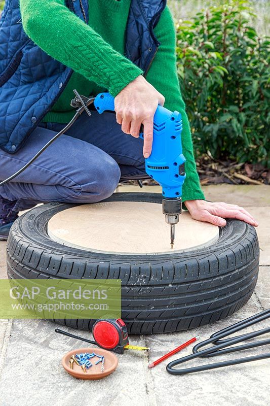 Woman using electric screwdriver to attach plywood disk to tyre