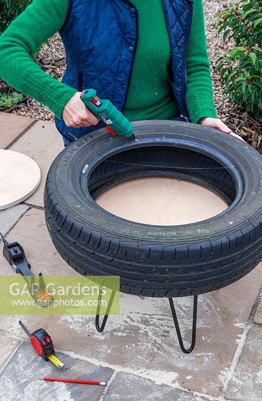 Woman using glue gun to apply a bead of glue around rim of car tyre