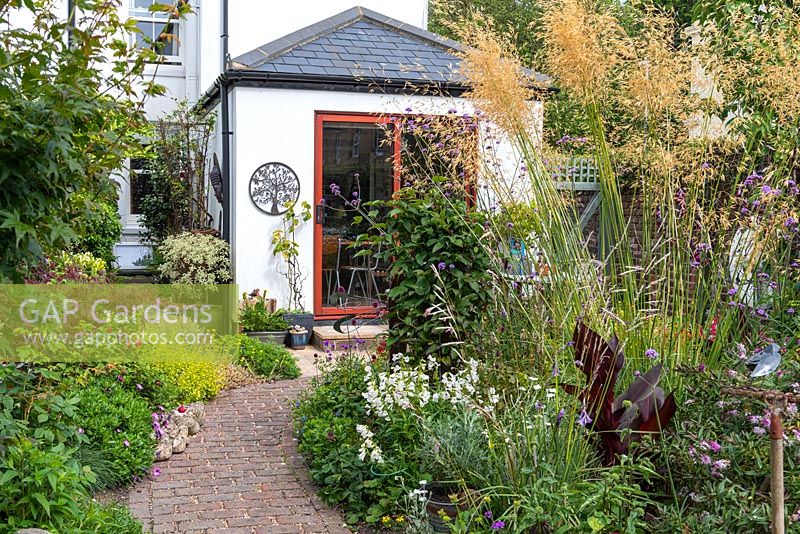 View back to rear extension, past clump of Stipa gigantea, Verbena bonariensis and cannas on right, to herb garden on left. 