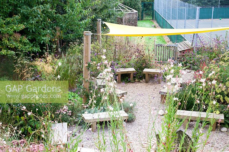 Wooden seating area for pupils and staff to enjoy amongst late summer planting. Sedlescombe Primary School, Sussex, UK. 