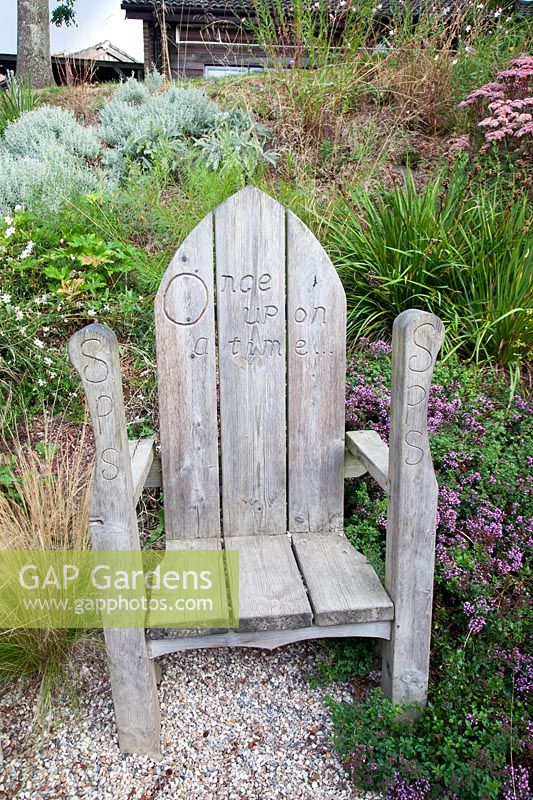 Engraved decorative wooden child's seat amongst late summer planting. Sedlescombe Primary School, Sussex, UK. 