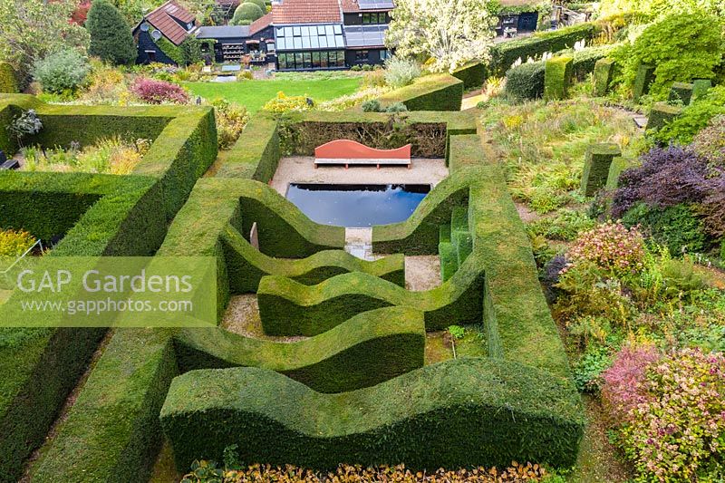 View over hedge gardens to house. Hedges of clipped Taxus baccata - Yew - enclosed wavy lines of hedge and a reflecting pool