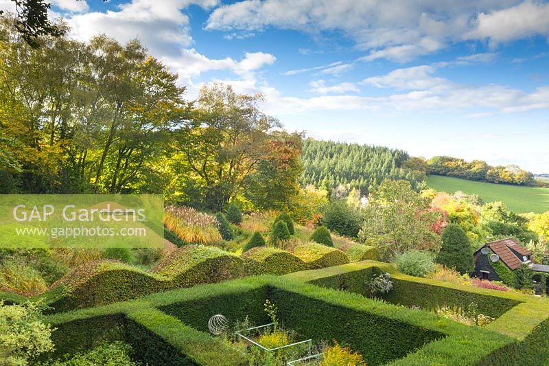View over hedge garden with wavy and formal hedges to countryside of trees and hills