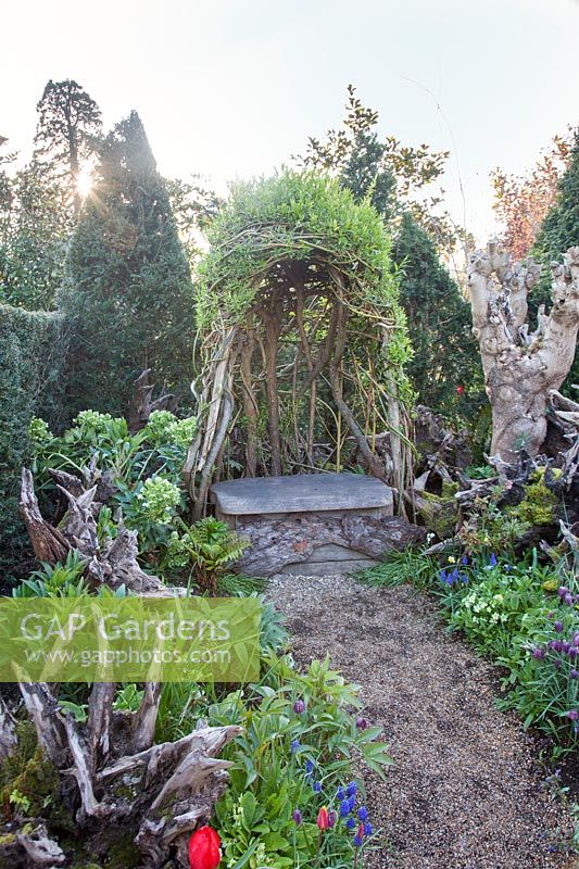 The Stumpery garden with decorative sculptural logs, a living sculpture seat and Muscari, fritillary, ferns and hellebores. Arundel Castle, West Sussex, UK.
