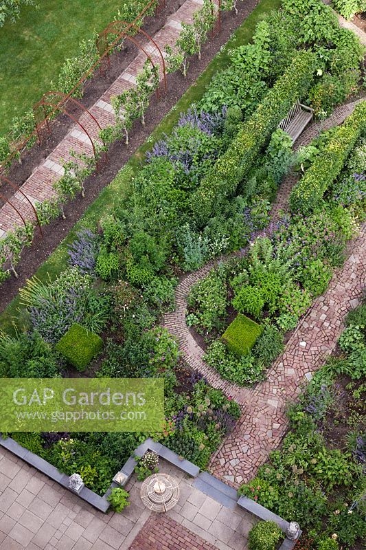 Aerial view of garden with flowerbeds and fruit trees trained on archway linked by brick and stone pathways - Holland, June