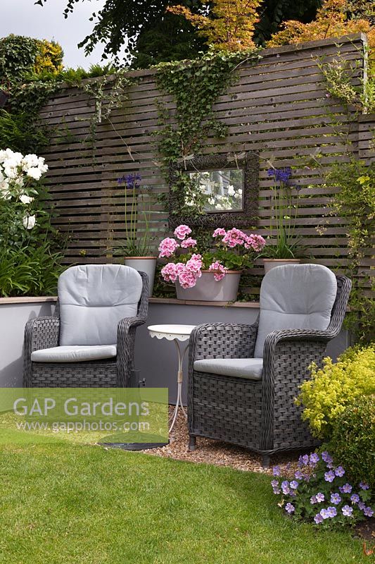 Grey rattan chairs in front of grey painted wall by lawn