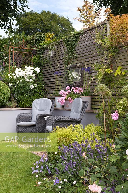 Grey rattan chairs in front of grey painted wall by lawn in cottage garden