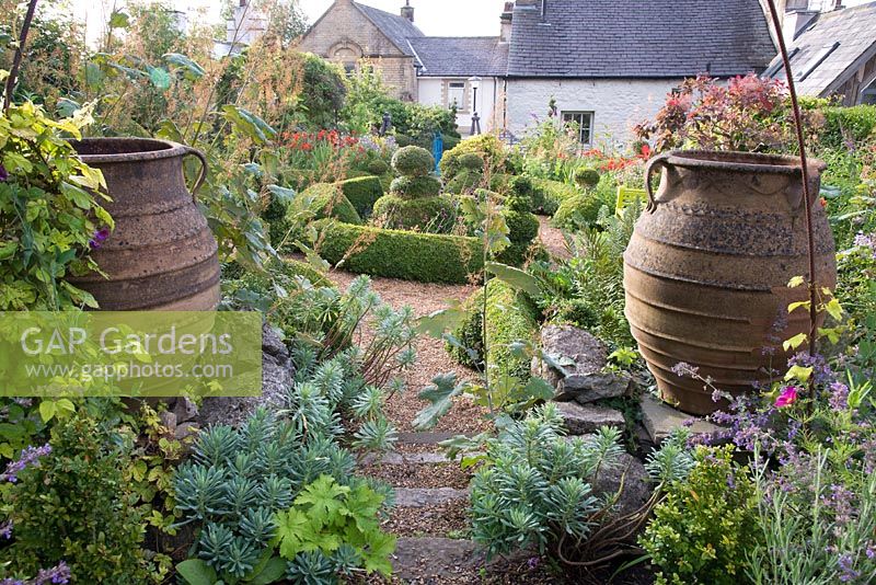 Overview of cottage garden with topiary, large urns and informal borders.
