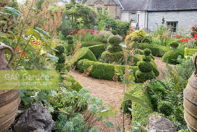 Overview of cottage garden with topiary, large urns and informal borders. 