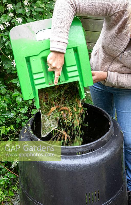 Mixing grass clippings with soil when adding to a compost bin.