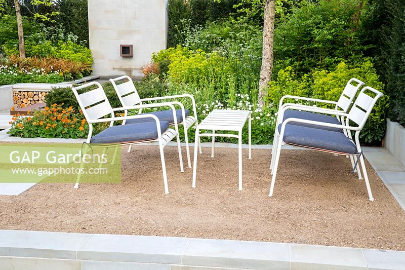 White metal framed table and chairs with blue cushions on crushed stone gravel seating area. The Sunken Retreat. RHS Malvern Spring Festival, 2016. Design: Ann Walker for Graduate Gardeners
