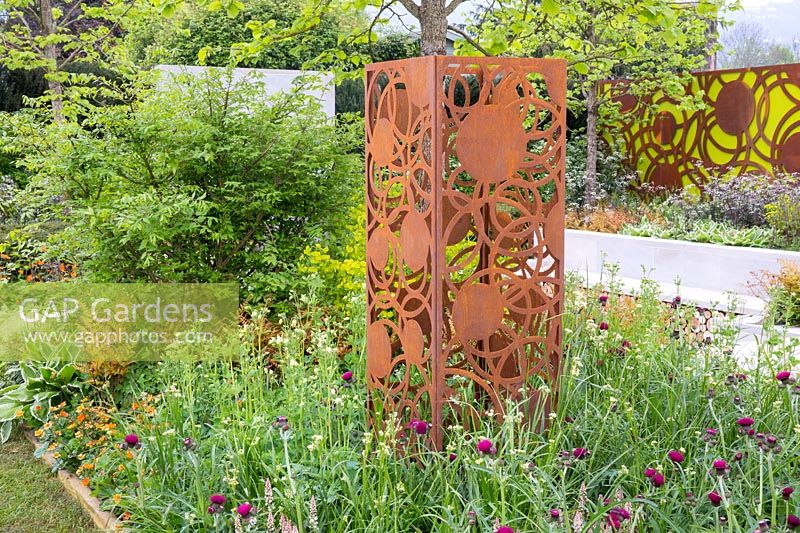 A corten steel rusted sculpture on a mixed flower border. The Sunken Retreat. RHS Malvern Spring Festival, 2016. Design: Ann Walker for Graduate Gardeners