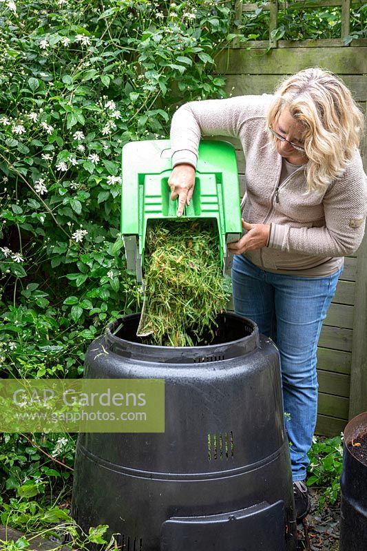 Mixing grass clippings with soil when adding to a compost bin.