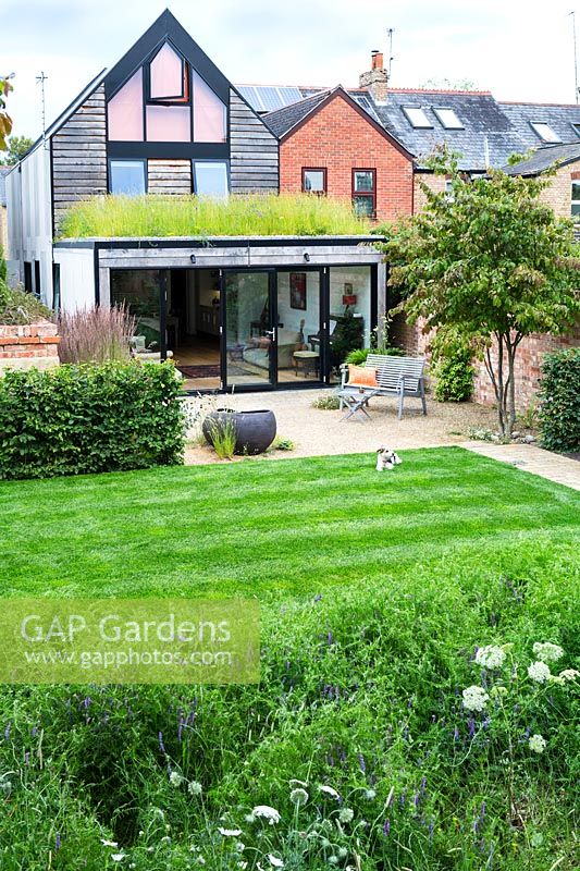 A modern house and garden with green roof, lawn, graveled seating area and contemporary pond.