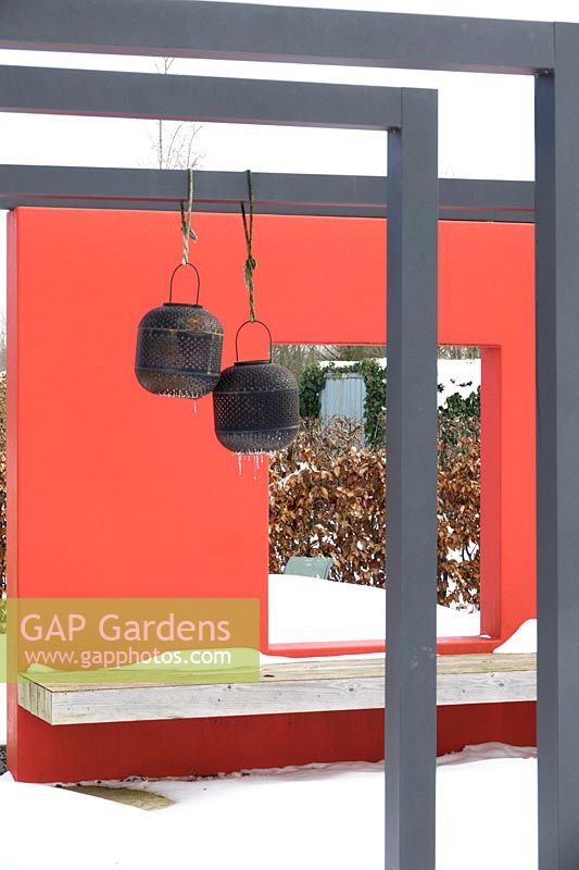 Two lanterns in garden designed by Tuin Ontwerp Buro Vught with red fences in the snow.