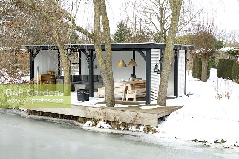 Summerhouse with comfortable lounge furniture near frozen lake in the middle of snow covered ground