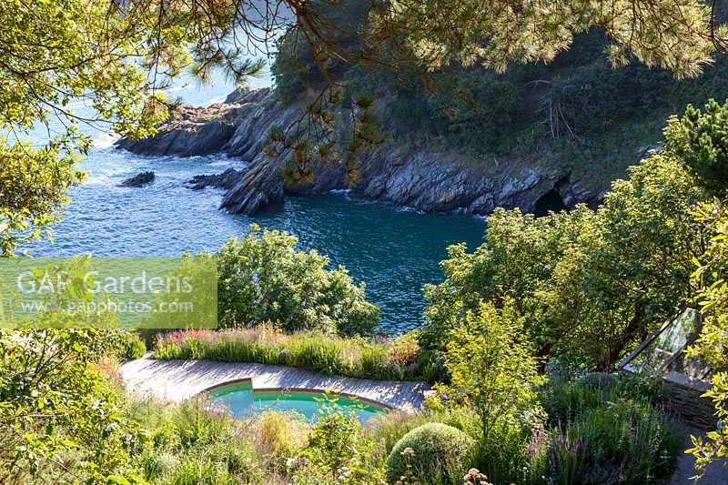 Looking down on planting surrounding swimming pool on garden on cliff, view of sea below