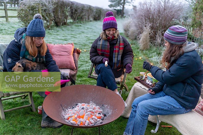 Women and dog sitting around a fire in a corten steel fire pit, keeping warm on a frosty winter day.