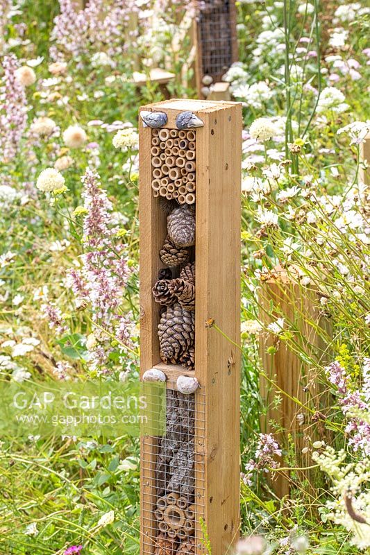 Vertical insect hotel towers in wildlife garden surrounded by wildflowers. Springwatch Garden, Hampton Court Flower Show, 2019.