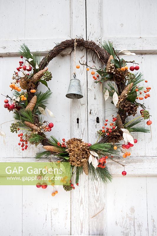 Pine wreath of berries, cones, seed heads and metal bell, hanging on a rustic wooden door