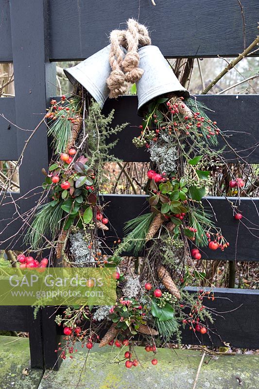Rustic Christmas wreath made with a mix of rosehips, crab apples, pinecones and foliage hanging from two metal bells. Styling: Marieke Nolsen