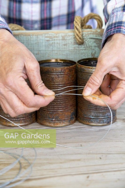 Women tying garden wire around tin cans to keep them properly fastened to the wooden board
