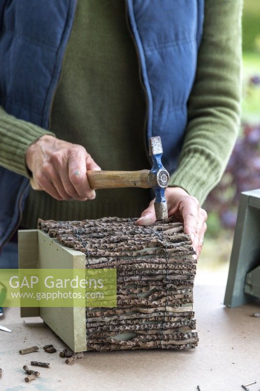 Woman hammering a nail into the bird box to keep the twig ladder in place