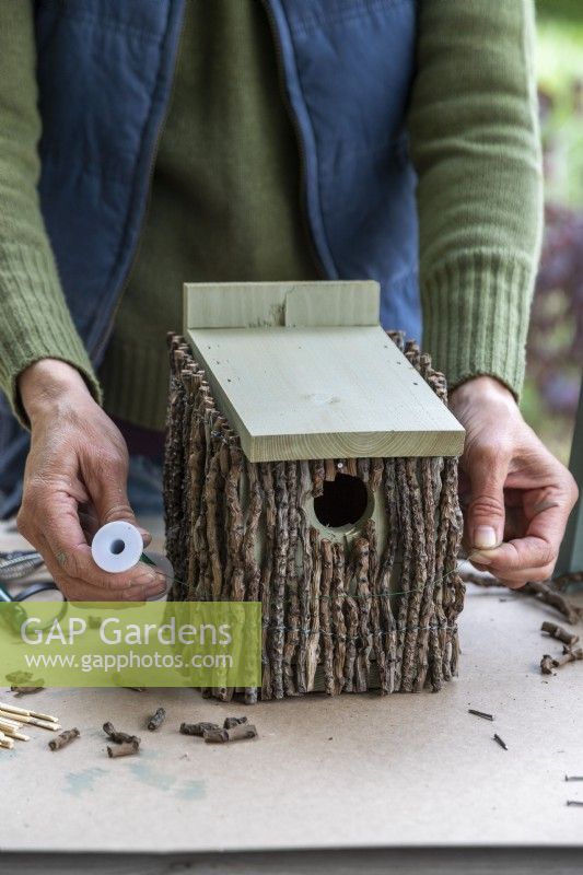 Woman wrapping wire around the birdhouse to keep the twigs in place