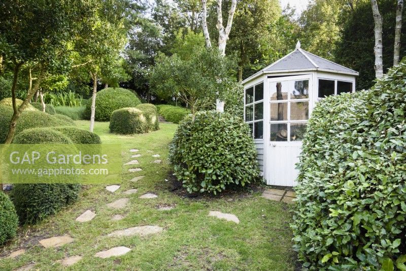 Small summerhouse framed by clipped Eleagnus x ebbingei in a garden made largely of green plants including clipped Lonicera nitida at Dip-on-the-Hill, Ousden, Suffolk in August