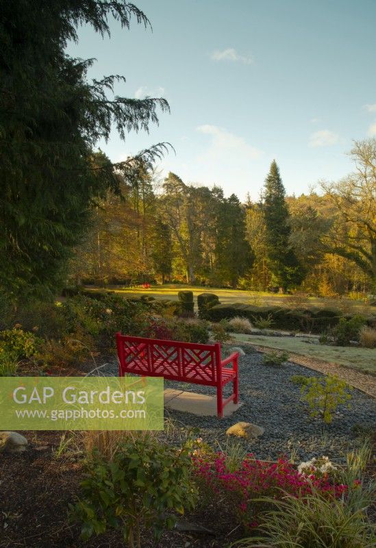 A Chinese red painted bench surrounded by plants in a viewing spot overlooking the garden at High Moss