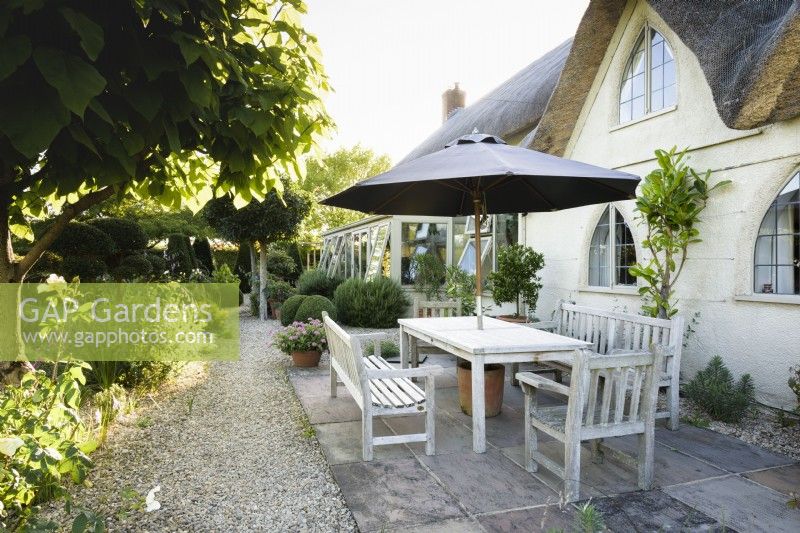 Dining area under umbrella in July outside a thatched cottage.