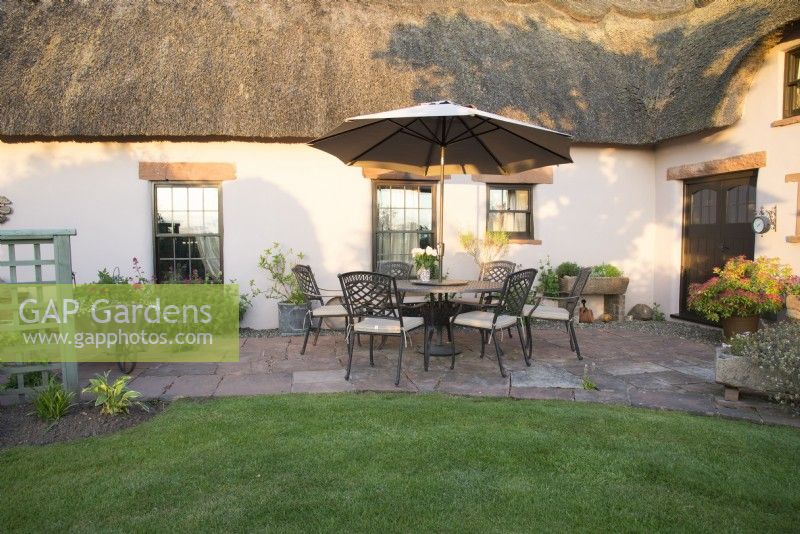 Stone patio with seating area outside thatched cottage