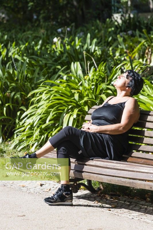 Woman on bench sunbathing. Estrela district, Lisbon, Portugal, September. 