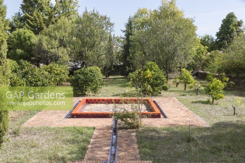 The citrus orchard in the lower garden. Square raised pool without water surrounded by geometric shaped brick paving. Lisbon, Portugal, September.