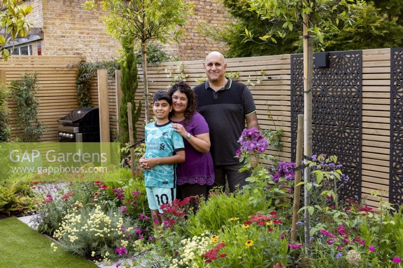 Couple with son standing near flower beds in a suburban garden