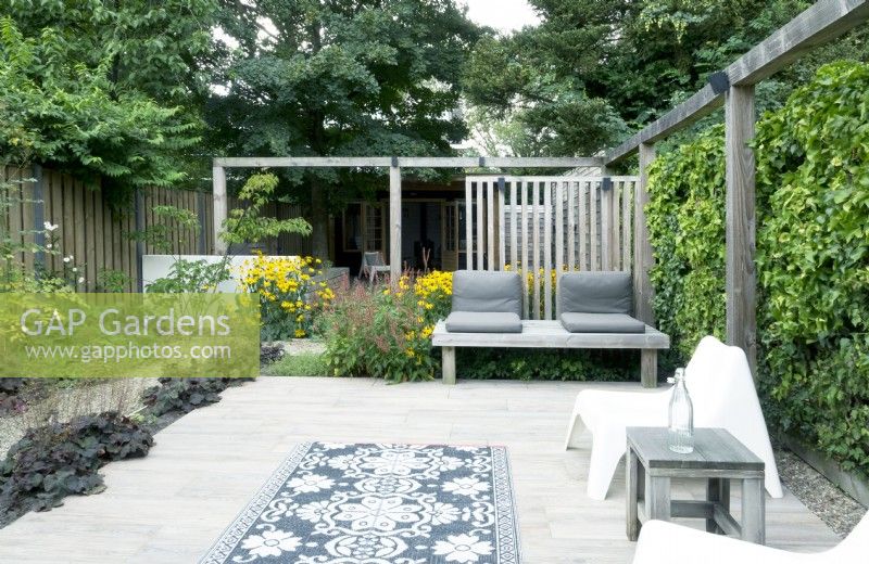Terrace with wooden pergola, wooden benches and garden carpet.