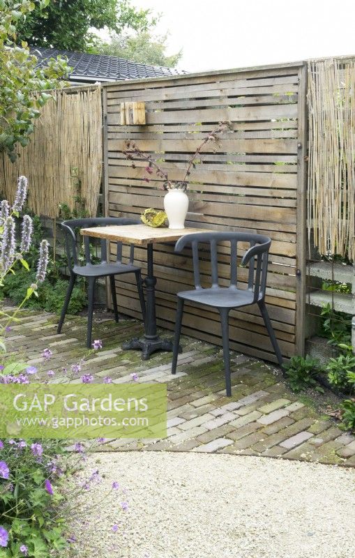 Slatted fence panel with table and chairs in front.