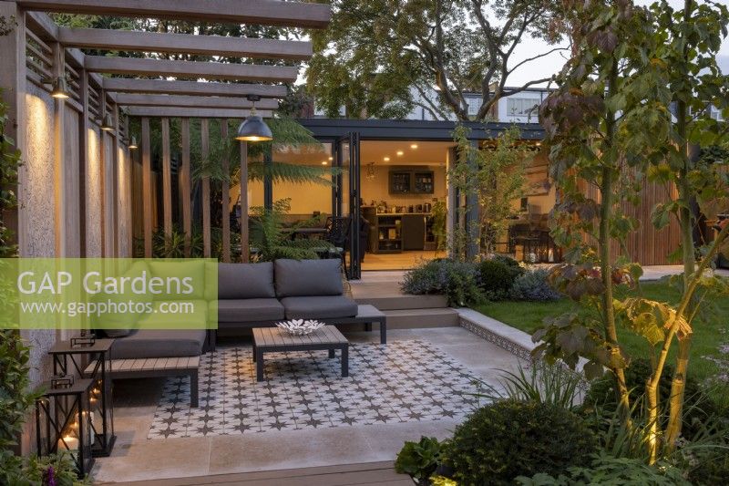 Modern garden patio and pergola at night with lighting, looking towards garden room or office