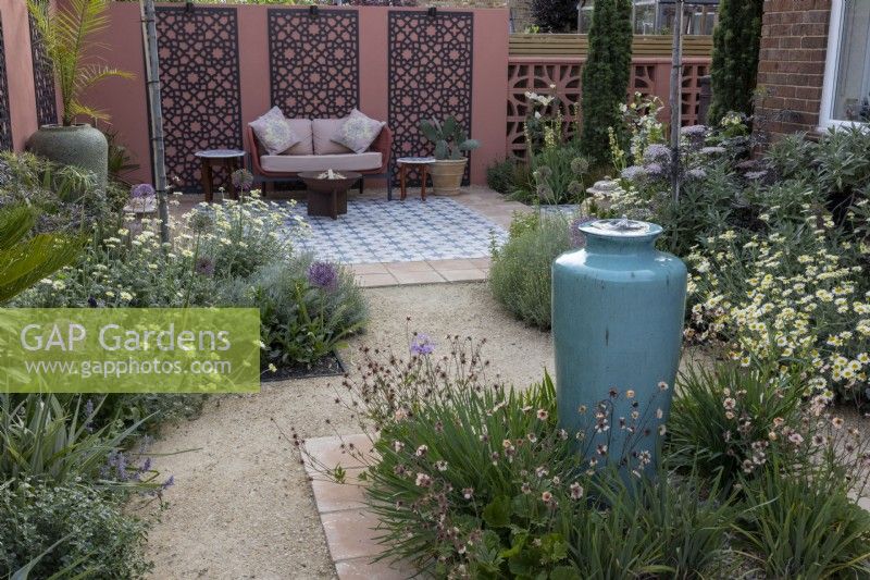 Contemporary gravel garden in suburban garden with tall ceramic container water feature and Moroccan style patio