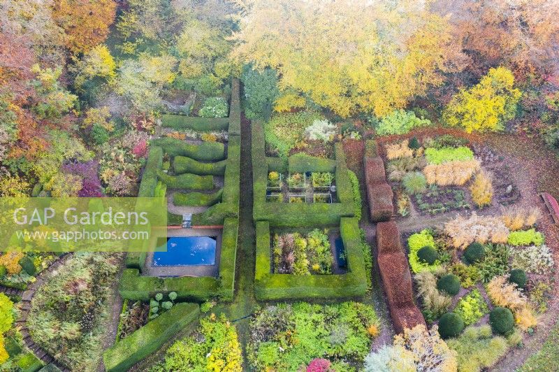 View over mature hedges of clipped Yew defining several garden rooms. Wave form hedge of Beech on right with large area planted with several different ornamental grasses in blocks; image taken with drone. November. Autumn.