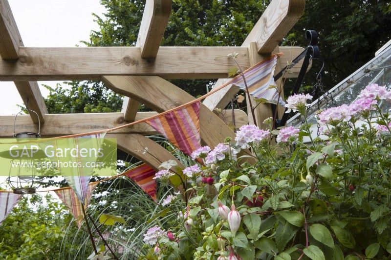  Detail of wooden arch used to hang bunting, a lamp and fitted with a bracket to support a planted hanging basket. Coombe Cottage garden. An NGS garden. July. Summer. 