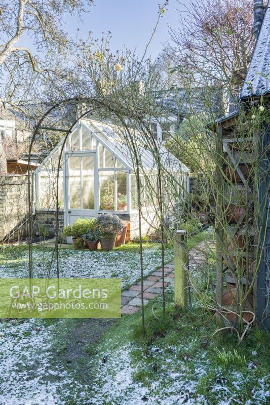 View through rose arch to traditional style painted timber greenhouse in winter. January