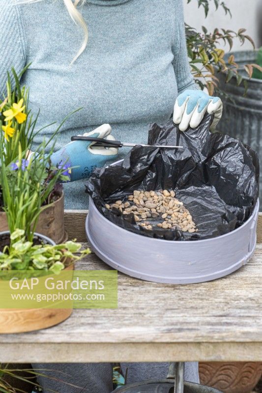 Step-by-Step Planting Wooden Flour Sieves with Spring Flowers. Step 3: line the sieve with black plastic, puncture in several places for drainage, and cover in gravel.
