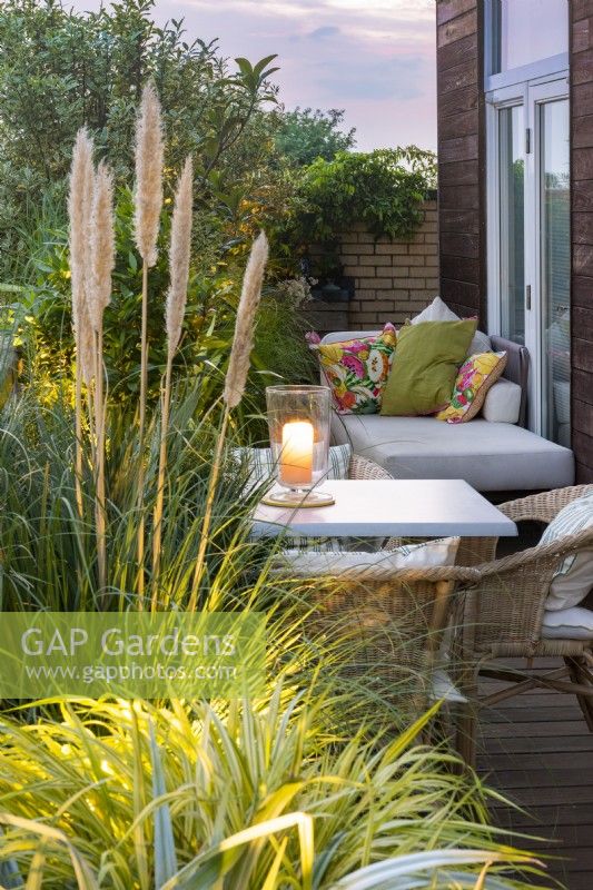 A balcony dining area is sheltered by planters of evergreen  pittosporum, loquat and olive trees, interspersed with ornamental grasses and pampas grass.
