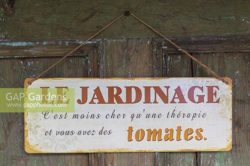 French language Le Jardinage sign hung on a door with proverb that reads gardening costs less than a therapy and you have tomatoes, Quebec, Canada