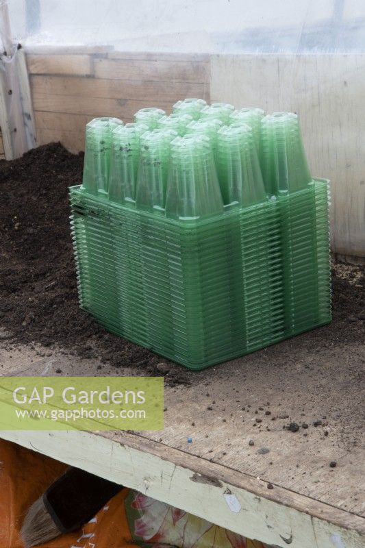 A bulk load of green plastic seed trays sit on a potting bench beside a pile of compost in a small commercial nursery. 