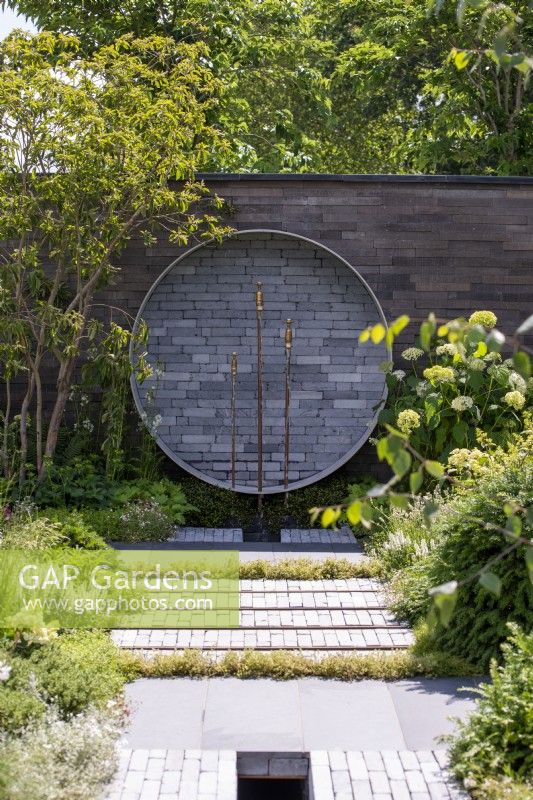 Clay paver path leading to a circular water feature with brass taps.  A Place to Meet Again - RHS Hampton Court Garden Festival 2021. 
Design: Mike Long - Sponsors: Association of Professional Landscapers, Kebur Garden Materials, Creepers Nurseries, Landscape Plus