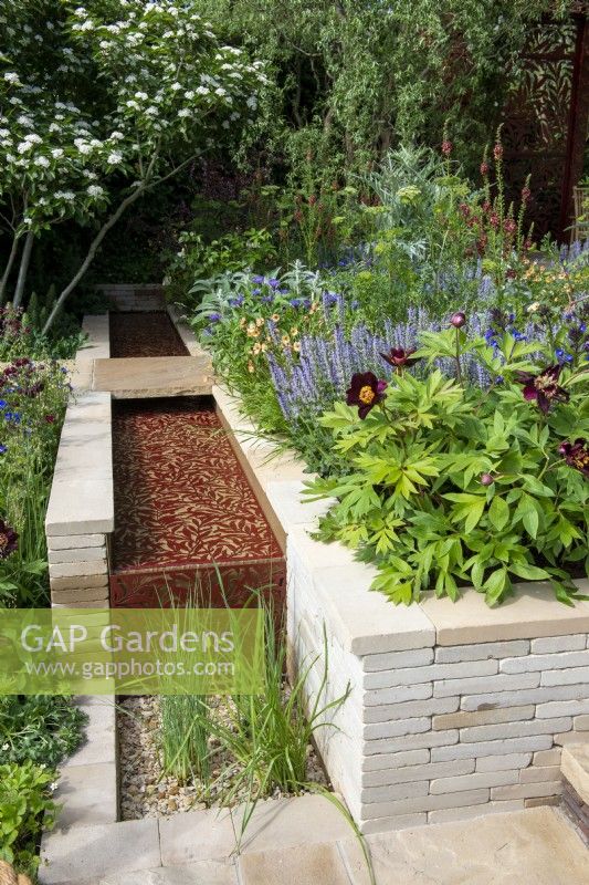 Water rill with laser cut willow pattern, clay paver raised bed with Paeonia 'Dark Eyes', Salvia 'Blue Hills', Verbascum and Geum - Morris  and  Co, RHS Chelsea Flower Show 2022 - Gold Medal
