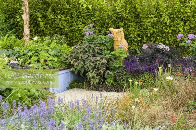 Green, purple, bronze and blue planting including Sambucus  'Black Beauty' Nepeta 'Summer Magic' and carex grasses  with wooden sculpture of Owl - SSAFA Sanctuary Garden