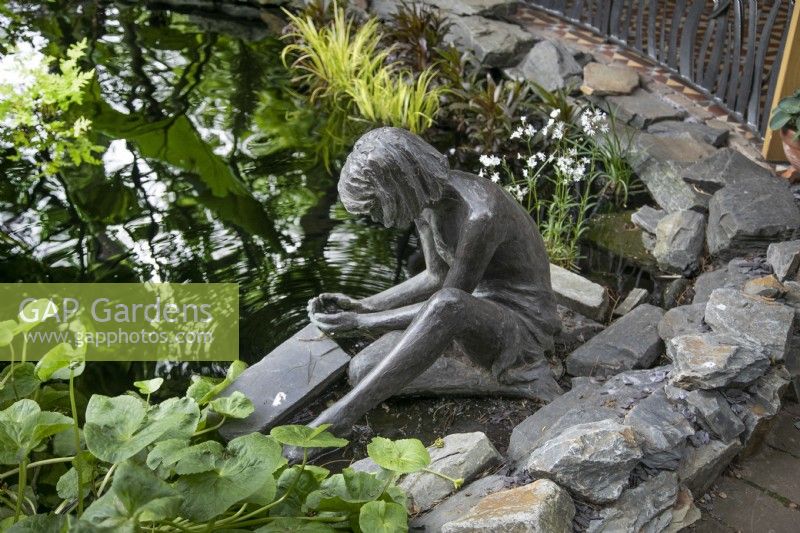 Bronze female sculpture sitting at the edge of the pond at Hamilton House garden in May 